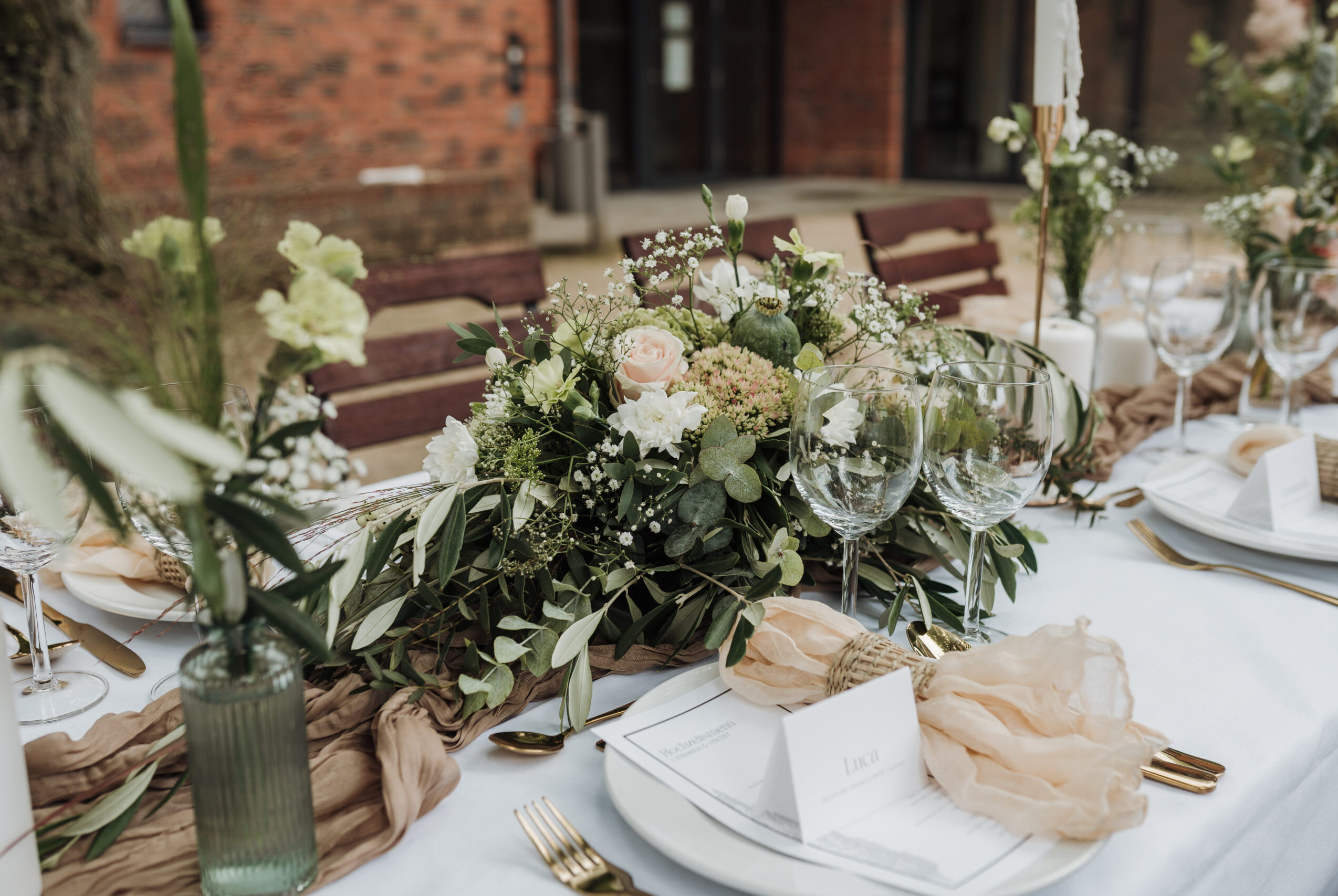 Festlich dekorierter Tisch im Freien mit Blumenarrangement und Gläsern unter Bäumen.